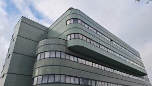 Het bestaande gebouw aan de Jan van Foreeststraat, ingezoomd op de bovenste etages. Het gebouw staat afgetekend tegen een blauwe hemel met wolken.