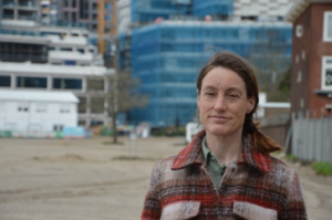 Op de voorgrond staat Marjo de Kraker, landschapsarchitect bij de gemeente Utrecht, met daarachter een open ruimte omgeven door hoogbouw.